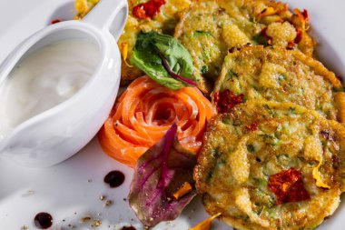 Fried fish in batter with salmon, basil, flower petals and caviar, lemon in a plate with sour cream in a sauce bowl in a plate