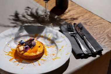 Pumpkin porridge in bread with blueberries, figs, cookies, seeds, flowers, and apricot pieces in a plate on the table with glasses of wine, cutlery, a vase with dried flowers, a tablecloth and a napkin on the background