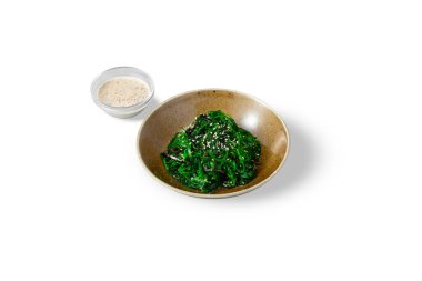 Chuka salad with sesame seeds in a plate and sauce in a bowl on a white background