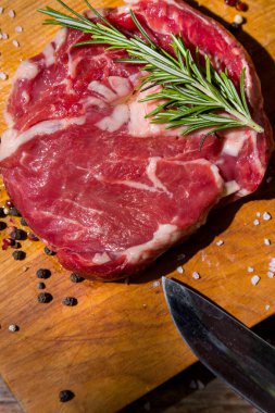 Çiğ domuz eti, defne yaprağı, biberiye, ahşap bir tahtada bıçaklı siyah biber ve ahşap bir masa. Dikey yönelim