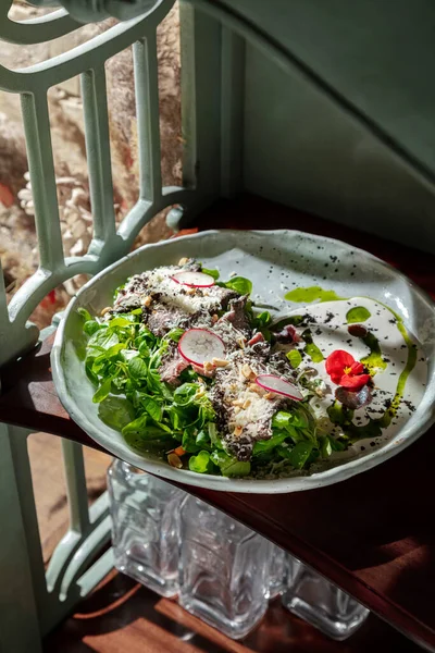 Fried meat with salad, parmesan, radishes, hazelnuts, mung bean salad, flower petals and tomatoes in a serving plate