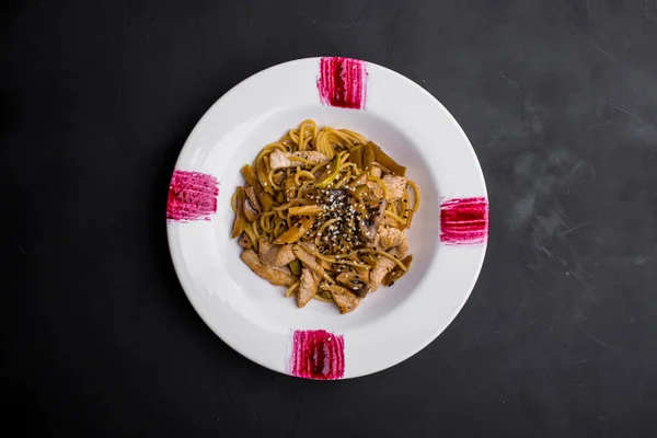 Spaghetti with meat, champignon, sesame seeds, zucchini and sauce in a plate on a dark stone background