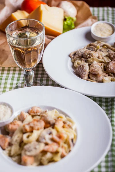 肉とパスタ シャンパン チーズ ワインのガラスとテーブルの上のプレートで 背景にチーズキューブとトマト — ストック写真