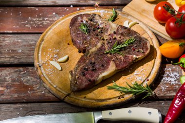 Kemikte ızgara et, sarımsak, domates, kırmızı sıcak ve tatlı biber, salatalık, biberiye, tuz ve biberli ahşap bir masa ve bıçakla birlikte. Yatay yönelim