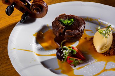 Cupcake with jam, strawberries, caramel, oatmeal cookies and a scoop of ice cream in a plate that stands on the table with a violin on the background