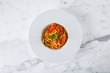 Domates soslu spagetti, biber peyniri ve mermer kaplama bir tabakta fesleğen.