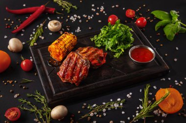 Fried pork steak with arugula, sauce and corn on a wooden board with mushrooms, peas, red chili peppers, salt, tomatoes and basil on a black background