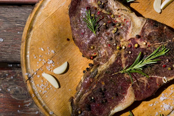 Kemiğin üzerinde ızgara et, ahşap bir tahta ve ahşap masa üzerinde sarımsak, biberiye, tuz ve biber. Yatay yönelim