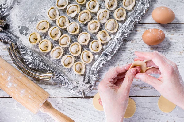 Raw dumplings on a baking sheet, sculpting dumplings with your hands, a rolling pin and an egg on a wooden background. Horizontal orientation