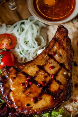 Çeri domatesli ızgara domuz bifteği, kiraz sosu, pide ekmeği, kırmızı biber, lahana ve salata bir bardak şarapla ahşap bir tahtada. Dikey yönelim 