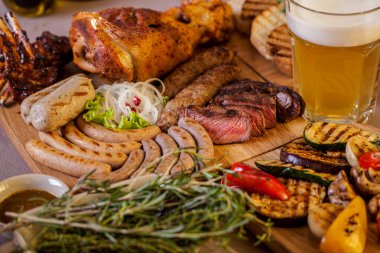 Domuz eti, kaburga, sosis, kebap, kabak, kiraz domatesleri, mantar, biber, ahşap bir tahtanın üzerinde turşulu ızgara ekmek ve bir bardak light bira. Yatay yönelim 