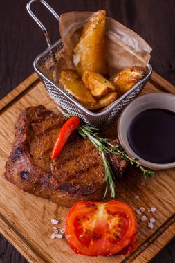Pork steak with pepper, salt, potatoes, tomatoes, rosemary, thyme, sauce on a wooden board. Vertical orientation 