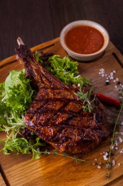 Beef steak on the bone with pepper, salt, frisee salad, french fries, thyme, pepper, endevia and red sauce on a wooden board. Vertical orientation 