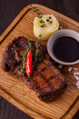 Pork steak with pepper, salt, mashed potatoes, thyme, sauce on a wooden board. Vertical orientation 
