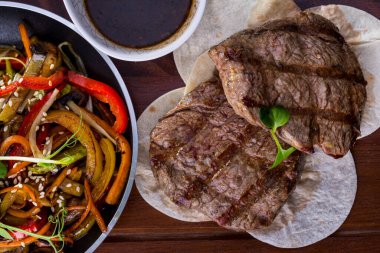 Grilled pork steak with sauce, marinated sauce, mung bean salad, pita bread, sesame seeds, asparagus and zucchini on a wooden table. Horizontal orientation 