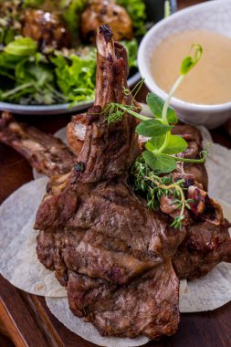 Grilled beef steak on the bone with sauce, mung bean salad, lavash, white sauce, on a wooden table. Vertical orientation 