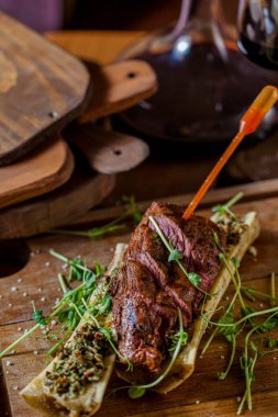 Grilled pork steak on a skewer with stuffed bone, mung bean salad, arugula with a glass of red wine on a wooden table. Vertical orientation 