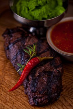 Grilled lamb on the bone, pea sauce, cherry sauce and rosemary on a wooden board. Vertical orientation 