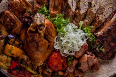Lamb on the bone, beef on the bone, cuts of pork, chicken tapaka, lula kebab, red chili, tomatoes, mushrooms, half onion, grilled zucchini and pita bread on a round platter. Horizontal orientation 