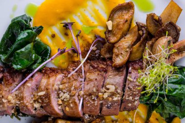 Grilled pork steaks with sprouts, spices, lemon slices, spinach and yellow gravy on a white plate. Horizontal orientation 