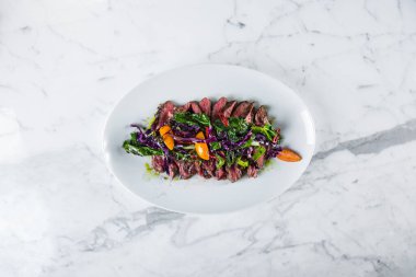 Grilled pork steaks with purple salad, kumquat, red chili and spinach on a white oval plate. Horizontal orientation 