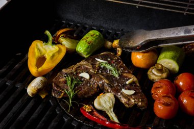 Grilled beef steak on the bone with rosemary, garlic, onion, pepper, zucchini, tomatoes lying on the embers. Horizontal orientation 