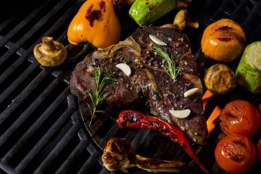 Grilled beef steak on the bone with rosemary, garlic, onion, pepper, zucchini, tomatoes lying on the embers. Horizontal orientation 
