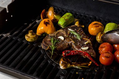 Grilled beef steak on the bone with rosemary, garlic, onion, pepper, zucchini, tomatoes lying on the embers. Horizontal orientation 
