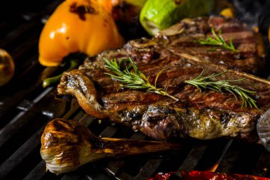 Grilled beef steak on the bone with rosemary, garlic, onion, pepper, zucchini, tomatoes lying on the embers. Horizontal orientation 