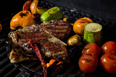 Grilled beef steak on the bone with rosemary, garlic, onion, pepper, zucchini, tomatoes lying on the embers. Horizontal orientation 