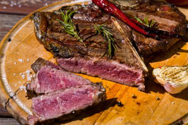 Pieces of beef on the bone grilled with rosemary, garlic, onion, pepper, zucchini, tomatoes lying on a round wooden board with salt. Horizontal orientation 