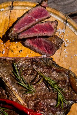 Pieces of beef on the bone grilled with rosemary, garlic, onion, pepper, zucchini, tomatoes lying on a round wooden board with salt. Vertical orientation 