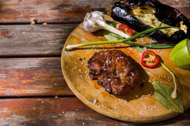 Grilled pork steak with garlic, leek, courgette, eggplant, bay leaf, and chili on a round board. Horizontal orientation 