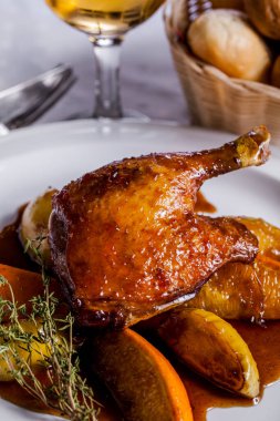 Grilled duck leg on the bone with thyme, lemon and sauce on a white plate, a basket of bread, a glass of wine. Vertical orientation