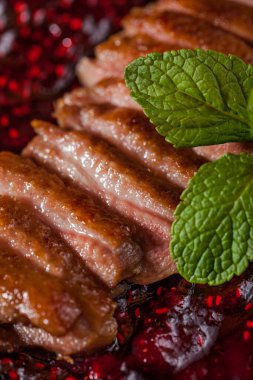 Grilled duck pieces with raspberry jam and mint on a plate and woody hay background. Vertical orientation