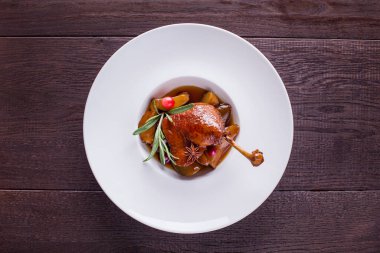 Grilled boneless duck leg with rosemary, badian, cherries and pear slices on a white round plate and on a wooden background. Horizontal orientation