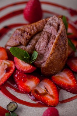 Grilled duck pieces in sauce with mint, raspberries, blueberries, strawberries and red caviar on a plate. Vertical orientation