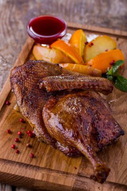 Grilled duck carcass in sauce with mint, orange and potatoes on a wooden board. Vertical orientation