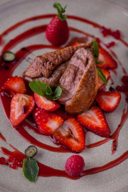 Grilled duck pieces in sauce with mint, raspberries, blueberries, strawberries and red caviar on a plate. Vertical orientation