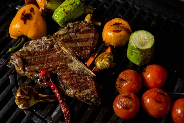 Grilled beef steak on the bone with rosemary, garlic, onion, pepper, zucchini, tomatoes lying on the embers. Horizontal orientation 