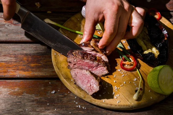 Barbecue beef cut with a knife into pieces with bay leaves, salt, red chili, garlic, zucchini and leeks lying on a round wooden board. Horizontal orientation