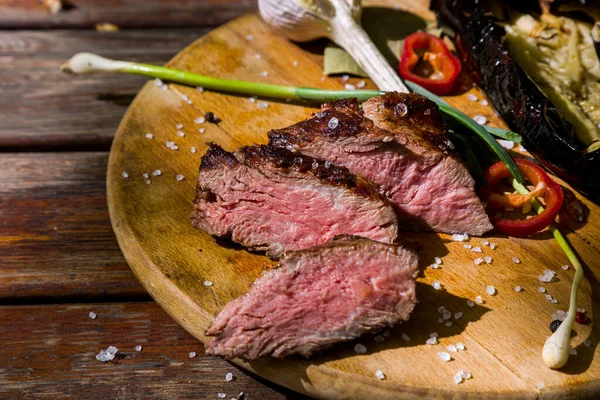 BBQ beef slices with bay leaves, salt, red chili, garlic, zucchini and leeks lying on a round wooden board. Horizontal orientation 