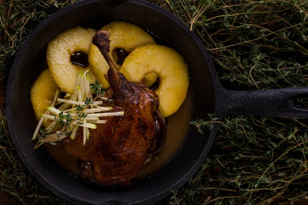 Grilled duck leg with bone, pineapple rings, thyme, grated apple in a cast iron skillet and thyme background. Horizontal orientation
