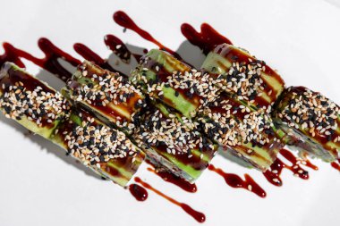 Roll green dragon in avocado. Sushi stuffed with salmon, eel, Japanese mayonnaise, cucumber and tobiko caviar, wrapped in nori seaweed, rice and avocado slices, unagi sauce is poured on top and sprinkled with white and black sesame