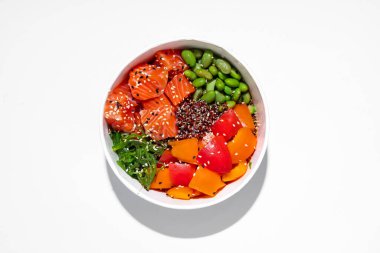 Bowl with salmon. On a white background in a white ceramic bowl lies green beans, quinoa, tomatoes, salmon fillet and chuka seaweed. Topped with white and black sesame seeds.