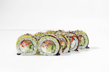 Roll green dragon in avocado. Sushi stuffed with salmon, eel, Japanese mayonnaise, cucumber and tobiko caviar, wrapped in nori seaweed, rice and avocado slices, unagi sauce is poured on top and sprinkled with white and black sesame