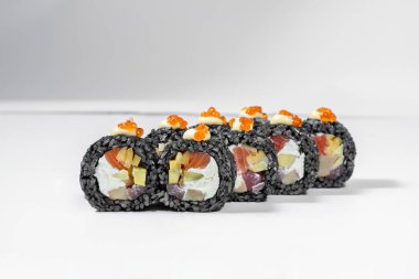 Black sushi roll with tuna and salmon. Fillet of tuna, salmon, cream cheese, tofu, avocado and mango, wrapped in nori seaweed and black rice with cuttlefish ink. On top of each piece is Japanese mayonnaise and red caviar. Sushi stands on a white back