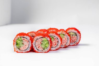 California sushi roll in tobiko with crab meat. Stuffing of snow crab meat, avocado and cucumber, wrapped in nori seaweed, rice with red tobiko caviar. Sushi stands on a white background.