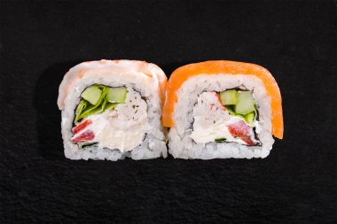 Rolls with salmon, shrimps, crab, pepper, onion, cucumber, rice and cream cheese on a black background