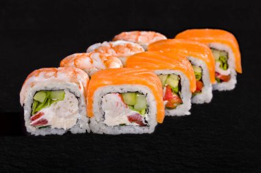 Rolls with salmon, shrimps, crab, pepper, onion, cucumber, rice and cream cheese on a black background